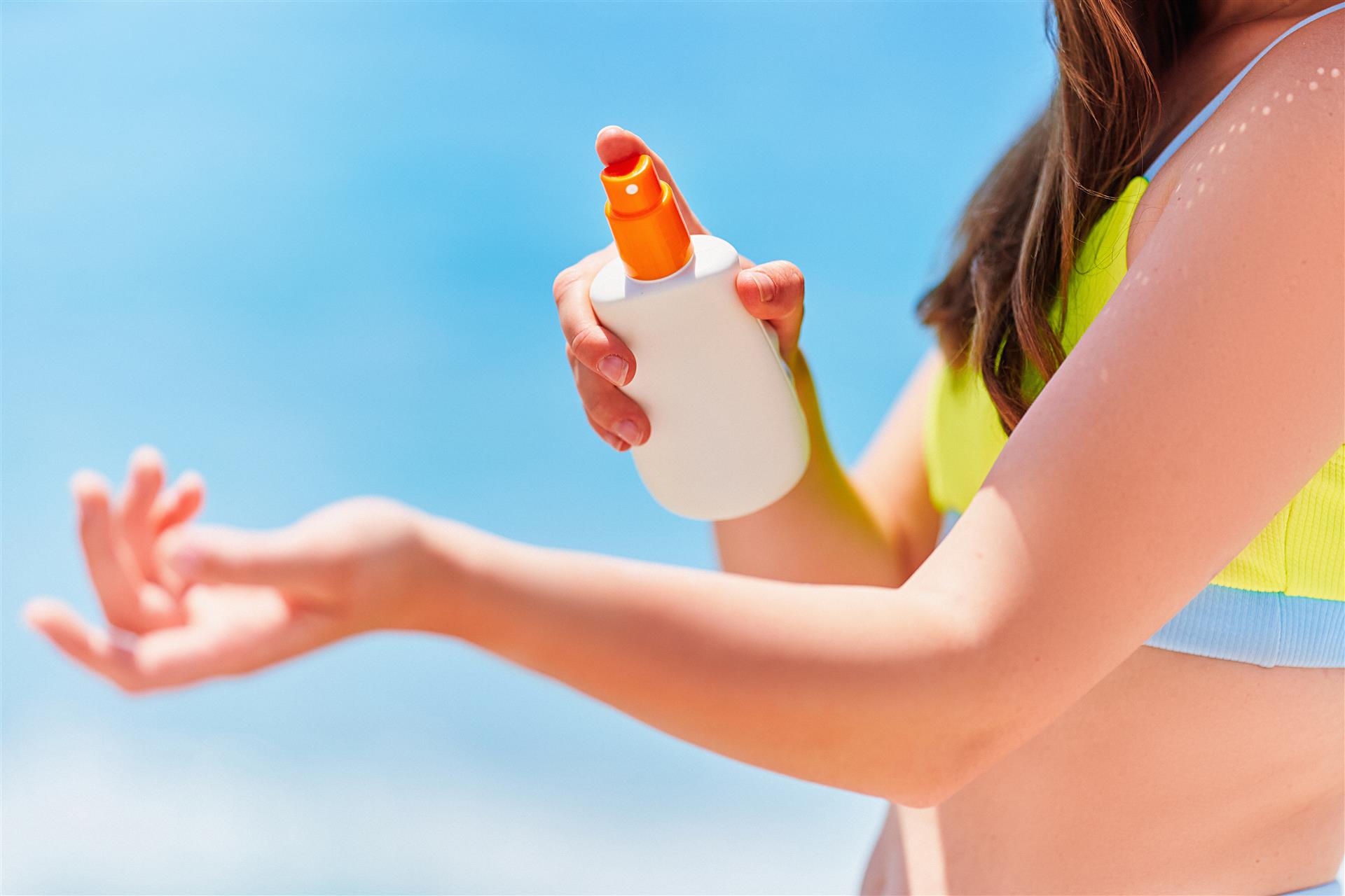 Female applying and holding white empty bottle blank of sunscreen lotion while sunbathing on beach by the sea in sunny summer day. Sun protection